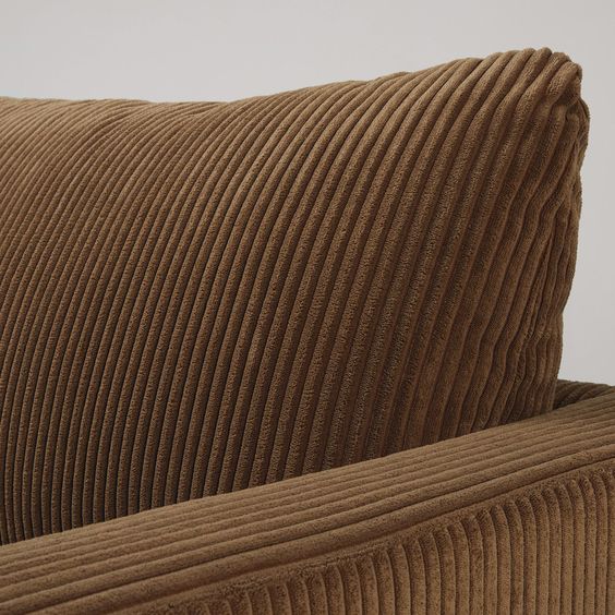 Zoom sur le coussin et l'accoudoir d'un canapé en velours côtelé marron. Un grand classique des années 70. 