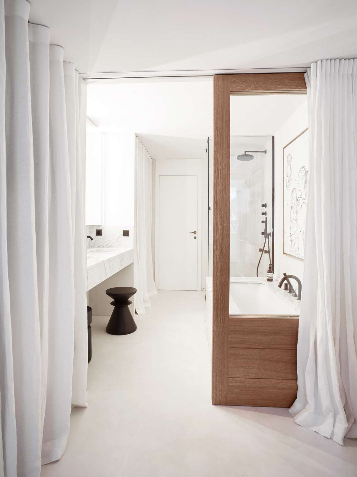 Salle de bain en longueur dans les tons de blanc et marron avec un évier un espace lavabo en marbre. Les vitres de la douche sont transparentes et bordurées par du bois rappelant la séparation de la chambre avec le reste de l'étage. 