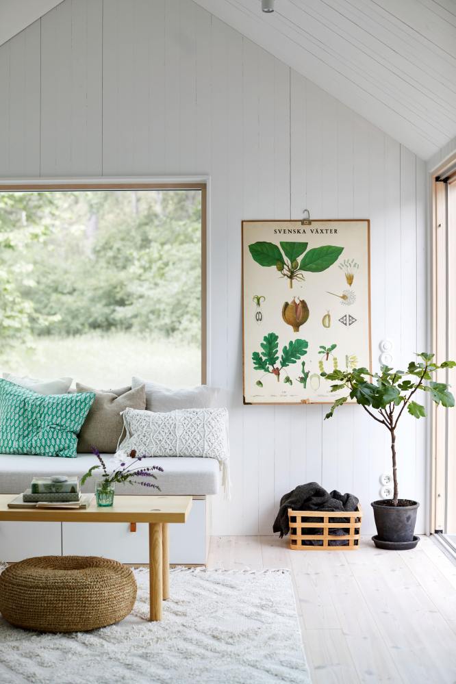 Tiny House en bois entièrement peinte en blanc avec des meubles en bois et en rotin pour qui appuient le côté rustique. Des larges fenêtres ouvrent sur l'extérieur et apportent la lumière naturelle.