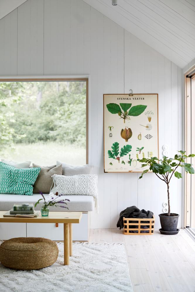 Tiny House en bois entièrement peinte en blanc avec des meubles en bois et en rotin pour qui appuient le côté rustique. Des larges fenêtres ouvrent sur l'extérieur et apportent la lumière naturelle. 