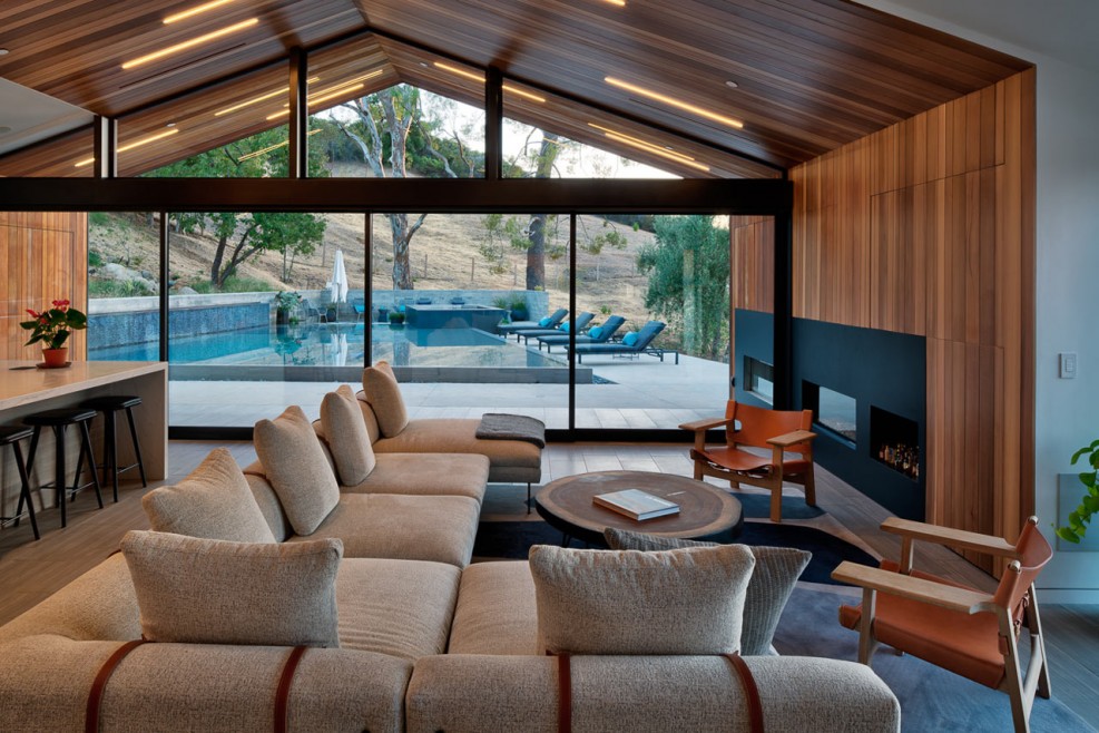 Vaste salon meublé avec un canapé d'angle couleur liège. La baie vitrée ouvre la vue sur la piscine et la nature environnante. CP. Grant Mudford