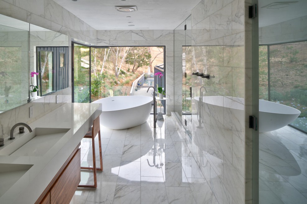 Salle de bain toute en marbre blanc avec une large fenêtre qui s'ouvre comme une porte derrière la baignoire pour se détendre dans son bain en aillant l'impression d'avoir un pied à l'intérieur et un autre à l'extérieur. CP. Grant Mudford