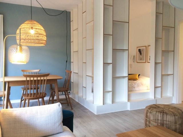Claustra d'interieur en bois peint en blanc pour séparer le séjour de la chambre. Il comprend aussi des espaces de rangements. 