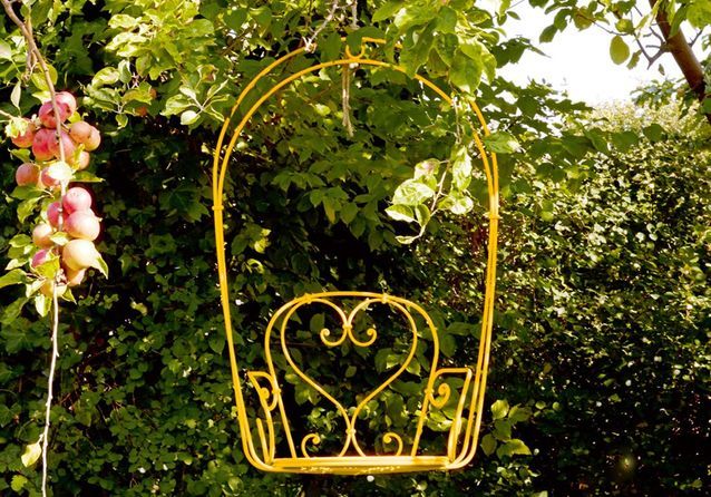 Fauteuil en fer jaune miel suspendu, idéal pour ajouter un aspect romantique à un jardin. CP. Fermob