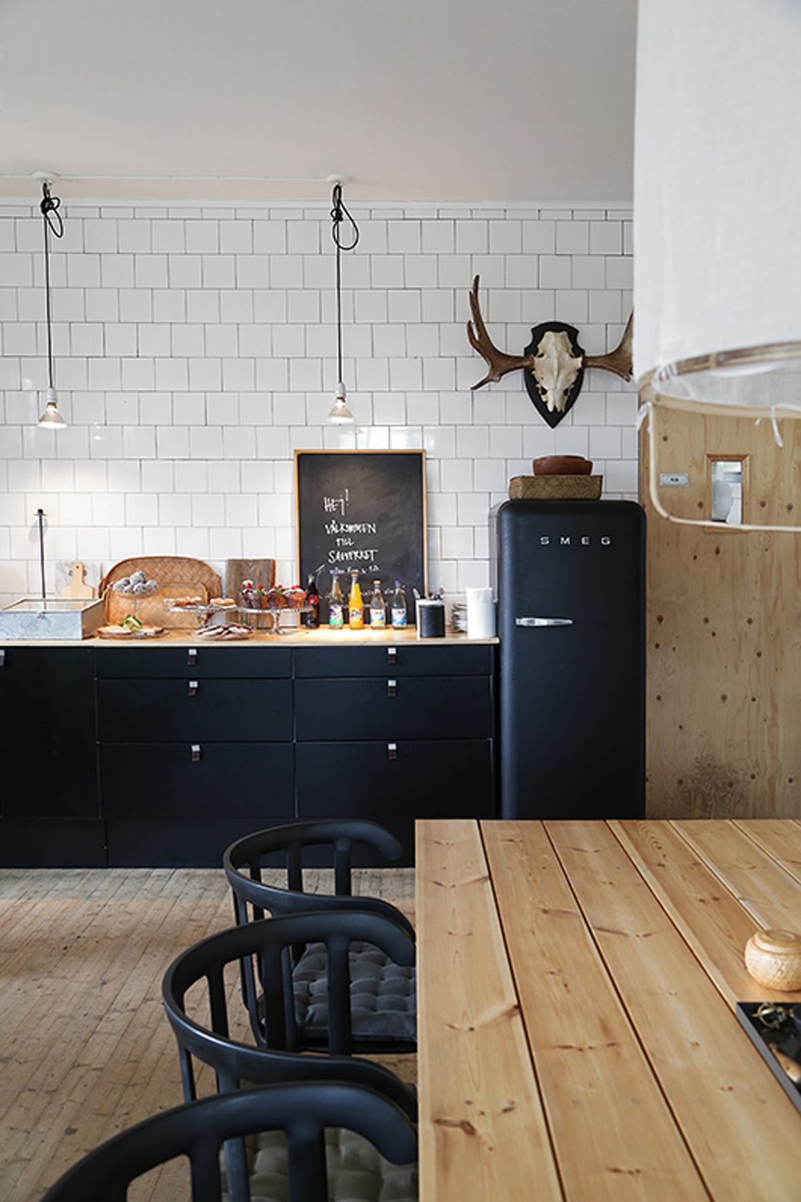 cuisine noire avec carrelage blanc au mur et une table à manger en bois et ses chaises noire
